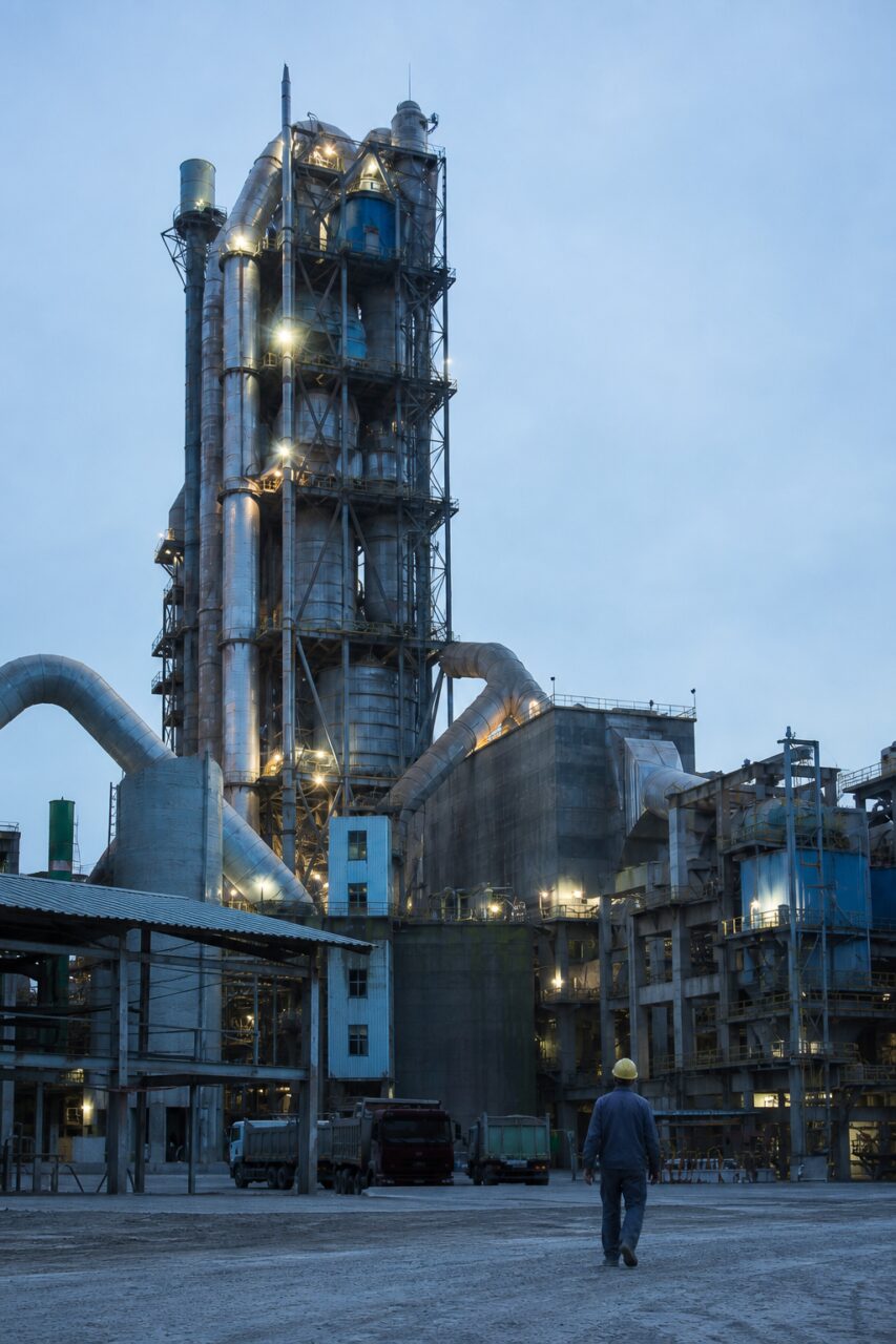 Avec longue ligne de bâtiments suivant les collines — Cimenterie avec four rotatif et silos