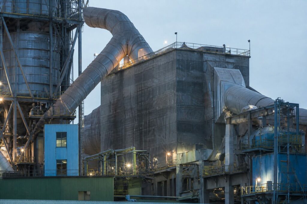 Avec structures et ciment baignés par la lumière du soir — Cimenterie avec four rotatif et silos