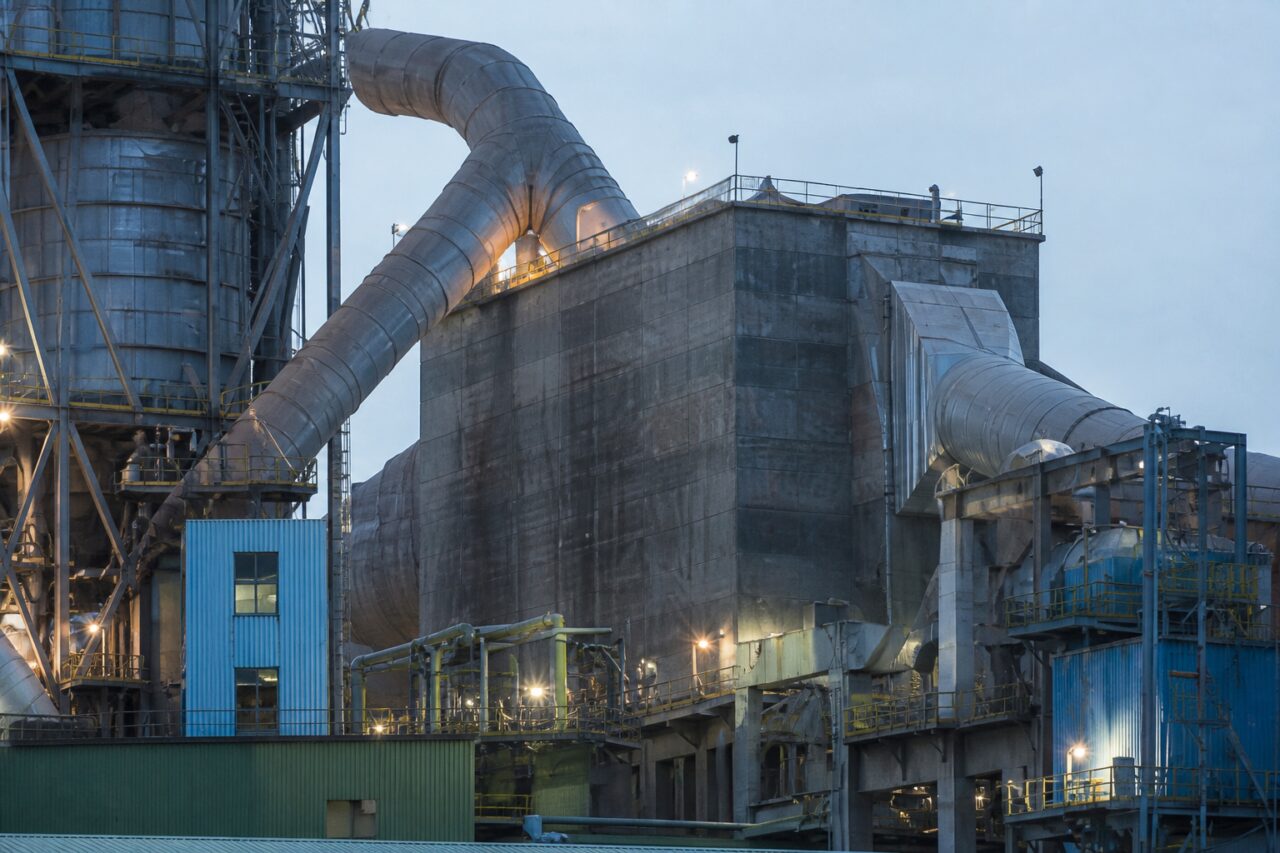 Avec structures et ciment baignés par la lumière du soir — Cimenterie avec four rotatif et silos