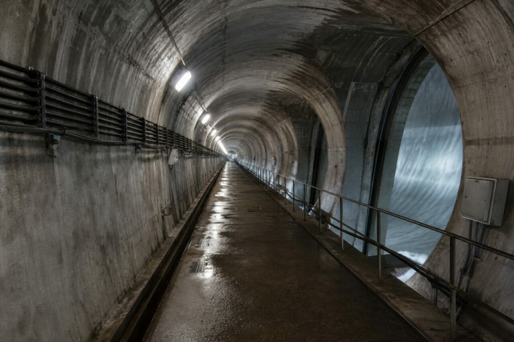 Barrage hydroélectrique et galerie d’inspection — Passerelle bétonnée, eau turbulente et câbles muraux