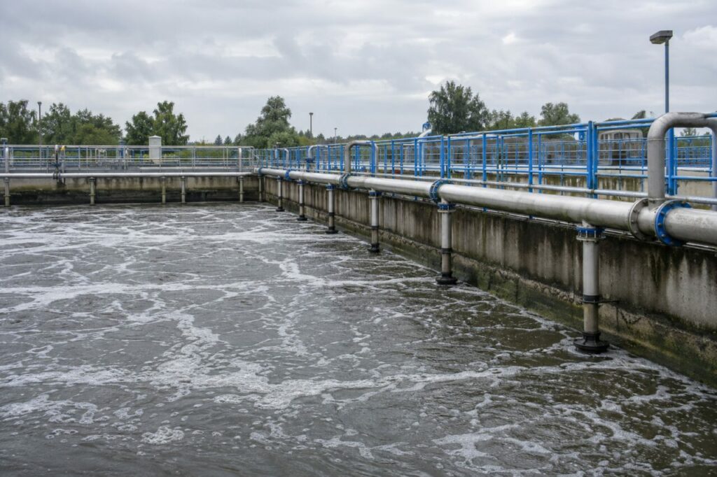 Bassin d’aération — un bassin rectangulaire d’aération avec diffuseurs de fines bulles, collecteurs inoxydables, garde-corps bleus et parois en béton dans une station d’épuration
