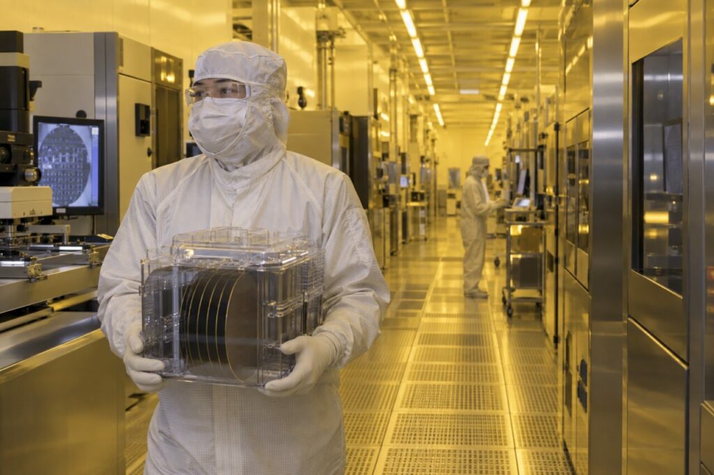 Couloir de salle blanche avec un technicien portant une cassette de wafers