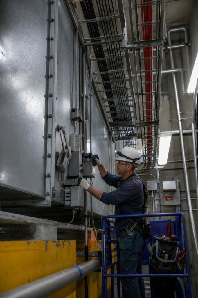Fire-damper maintenance in a technical gallery — beneath red and black cable trays