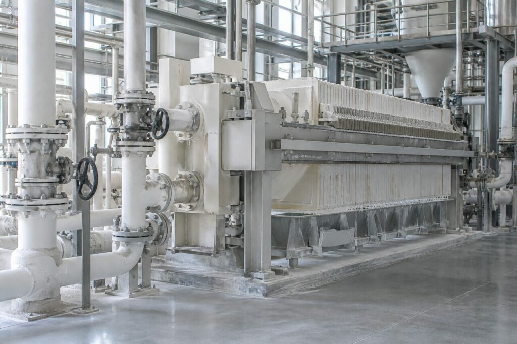Filtro-prensa industrial e tubagens claras numa fábrica de dióxido de titânio