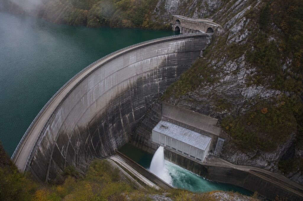 Retenue turquoise, voûte courbe et centrale en contrebas — Barrage hydroélectrique et galerie d’inspection